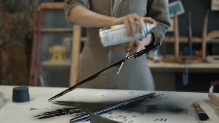 A female restorer spraying a wooden detail with black color can, female hands renew old wooden...