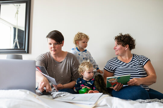 Lesbian couple and kids reading and working on bed
