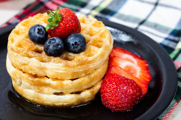 WAFFLES WITH STRAWBERRY BLUEBERRY AND SYRUP.