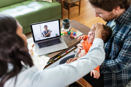 Couple with baby son video chatting with pediatrician on laptop screen