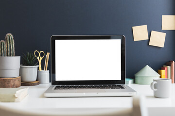 Fototapeta premium Desk with laptop mockup, stationery, Chinese money tree and books near navy blue wall. 