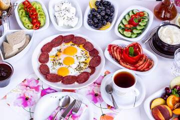 Traditional Turkish Breakfast with tomato,olives,honey,tea,cheese and egg with sausage on white surface.