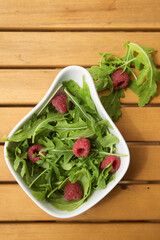 white deep dish with fresh arugula and raspberries. The concept of healthy eating