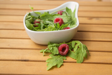 white deep dish with fresh arugula and raspberries. The concept of healthy food