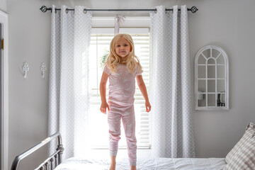 Cute little blonde girl jumping on big white bed