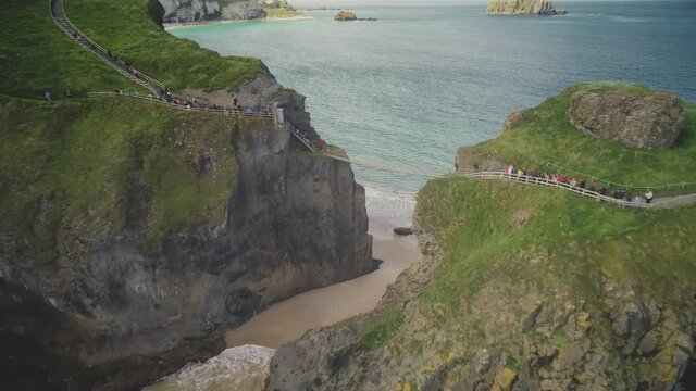 Irish people aerial: rope bridge Carrick-a-Rede in front of seascape. Picturesque landmark for daring tourists near Carrick islet, Northern Ireland. Cinematic footage shot in 4k, UHD