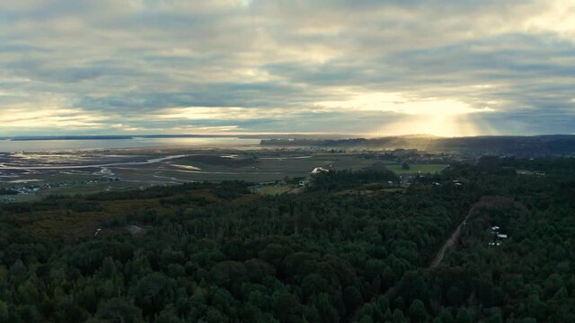 aerial view of wetlands and delta of the Chamiza river at its mouth to the bosom of Reloncavi, in a cloudy sunset with sun rays crossing the clouds