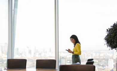 Businesswoman using smart phone in highrise conference room