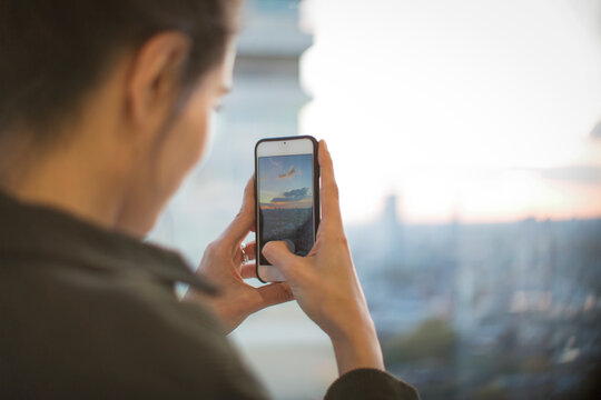 Woman with camera phone photographing sunset from highrise