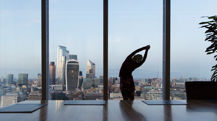 Businesswoman stretching at highrise office window, London, UK