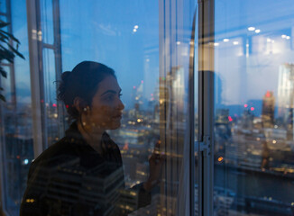 Thoughtful business woman working late at highrise office window