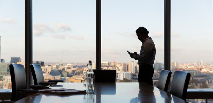Businessman using smart phone at highrise office window, London, UK