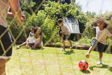 Happy family playing soccer in sunny summer backyard