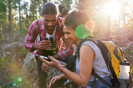 Happy young hiking couple using smart phone in sunny woods