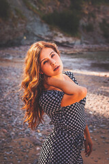 Fototapeta premium Sensual girl in a rocky cove wearing a black and white dots dress
