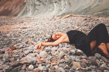 Girl with a black dress over a pile of little rocks in a cove from the basque coast.