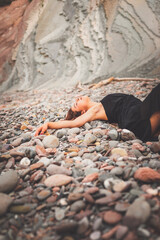 Girl with a black dress over a pile of little rocks in a cove from the basque coast.