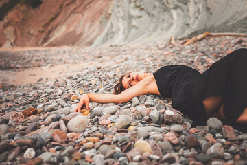 Girl with a black dress over a pile of little rocks in a cove from the basque coast.