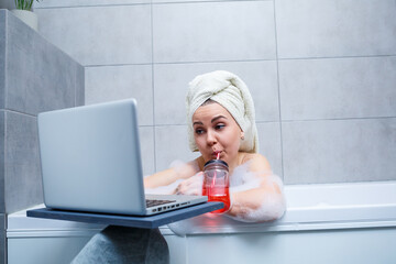 A young woman with a towel on her head drinks juice watching a movie on a laptop while sitting in a...