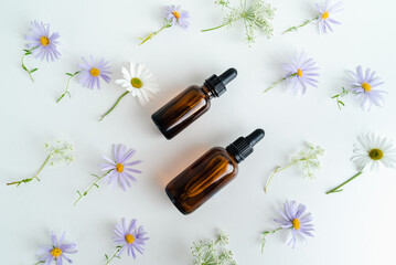 Bottles of essence and surum for skin health on  background of flowers. Natural herbal Skin care cosmetics in dark glass. Mockup advertising. 
Nourishing face oil