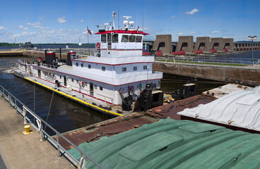 Pushing Barges:  A towboat moves three rows of covered barges through a lock and past a dam on the Mississippi River.
 - obrazy, fototapety, plakaty