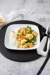A Vegan Stir-Fry with Cauliflower and Peas on a White Plate, Black Tray, Cement Table, topped with Peanuts