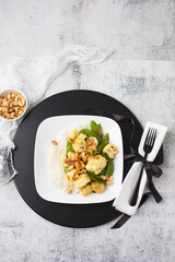 A Vegan Stir-Fry with Cauliflower and Peas on a White Plate, Black Tray, Cement Table, topped with Peanuts
