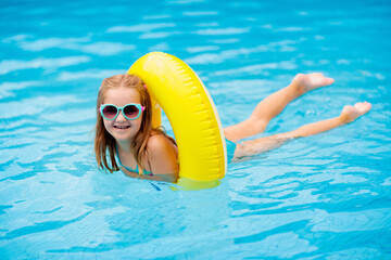 Child in swimming pool on toy ring. Kids swim.