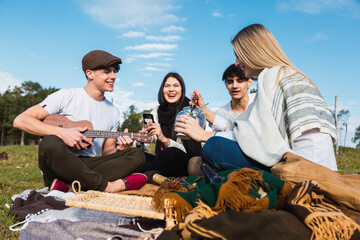 Group of friends enjoy a day in the country.  Woman drinking cup of mate infusion beverage.  The man plays ukulele and his friends smile.
