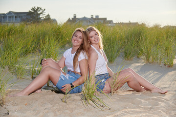 Two beautiful blonde sisters pose together for family photo on the beach - sitting near dune