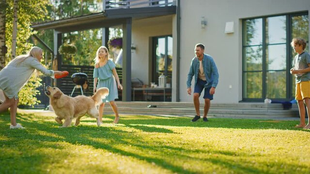 Smiling Beautiful Family of Four Play Fetch flying disc with Happy Golden Retriever Dog on the Backyard Lawn. Idyllic Family Has Fun with Loyal Pedigree Dog Outdoors in Summer House Backyard