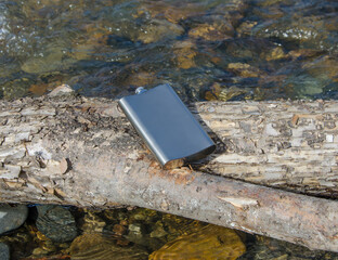 a metal water flask lying on a log near the river selective focus