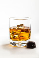 A glass of Kentucky bourbon on rocks with a chocolate candy isolated on white background