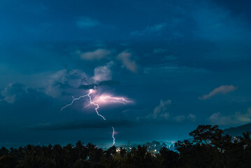 Lightnings, stars and dramatic clouds in the night sky over valley with trees, sea,  city and...
