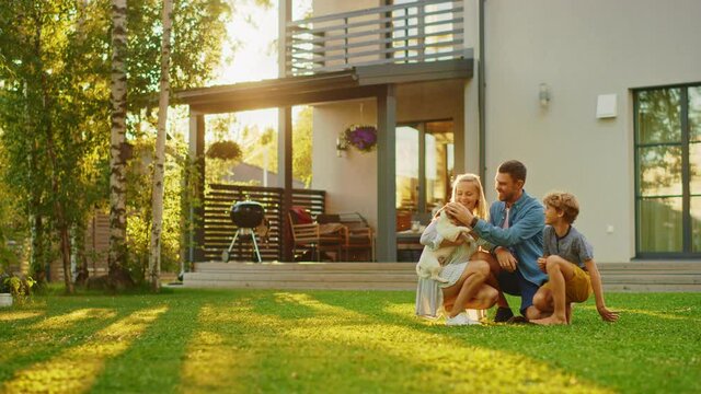 Smiling Father, Mother and Son Pet and Play with Smooth Fox Terrier Retriever Dog. Sun Shines on Idyllic Happy Family with Loyal Pedigree Dog have Fun at the Idyllic Suburban House Backyard