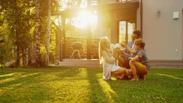 Smiling Father, Mother and Son Pet and Play with Smooth Fox Terrier Retriever Dog. Sun Shines on Idyllic Happy Family with Loyal Pedigree Dog have Fun at the Idyllic Suburban House Backyard