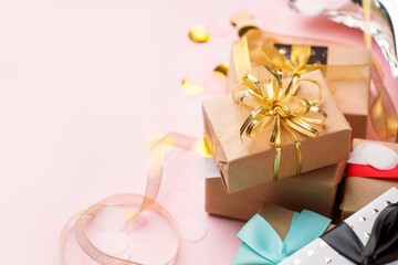 Holiday Luxury stylish gift present box wrapped in craft paper and tied with gold bows on pink background, decorated with confetti. Birthday, Christmas, New Year, Mother day, sale concept, copy space