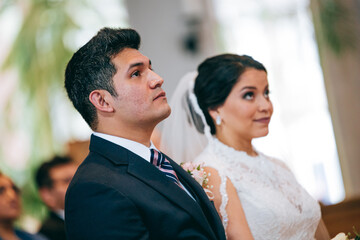Latino bride and groom focused on what the priest is saying