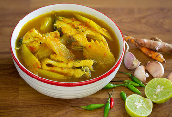 Sea bass in yellow curry with fresh papaya in white bowl on wooden table, Thai food