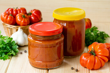 Homemade tomato hot sauce with garlic and pepper in glass jars on wooden table