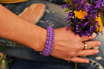 Braided paracord bracelet purple on a woman's hand on a summer day with flowers