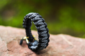 Braided paracord bracelet color black camouflage on the hand with a brass lock on a flat stone in the standing position clasp down right side
