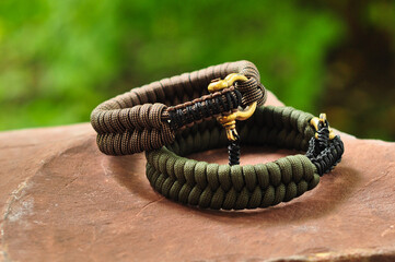 A braided paracord bracelet in khaki and brown on the hand with a brass lock on a flat stone in the...