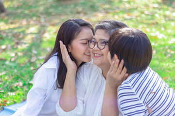 Asian lovely young daughter and grandson kiss happy and healthly senior woman or pleasure grandmother in moment of beautiful love in the park. Family generation relationship or bonding photo concept.