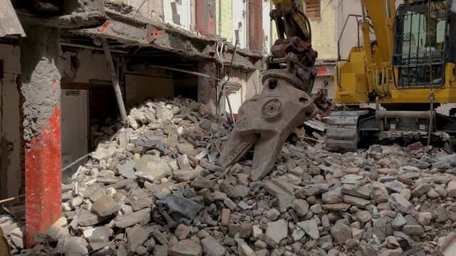 Demolition site of an old house, with an excavator on top of rubble in the middle of the gutted building with no roof or inner structure, panning right to left of the whole site