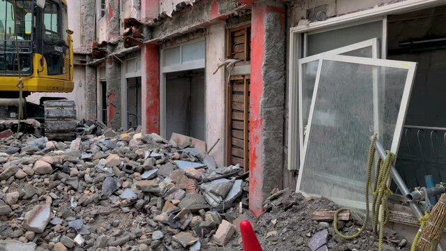Demolition site of an old house, with an excavator on top of rubble in the middle of the gutted building with no roof or inner structure, panning from right to the center where the excavator is.