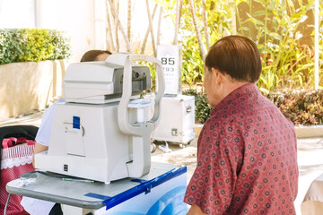 Elderly man checking eye vision on optometry equipment with a mobile hospital unit for eye...