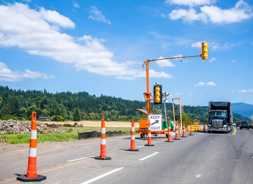 Black big rig semi truck with semi trailer standing on the temporary installed traffic light stop point of repairing section of the road