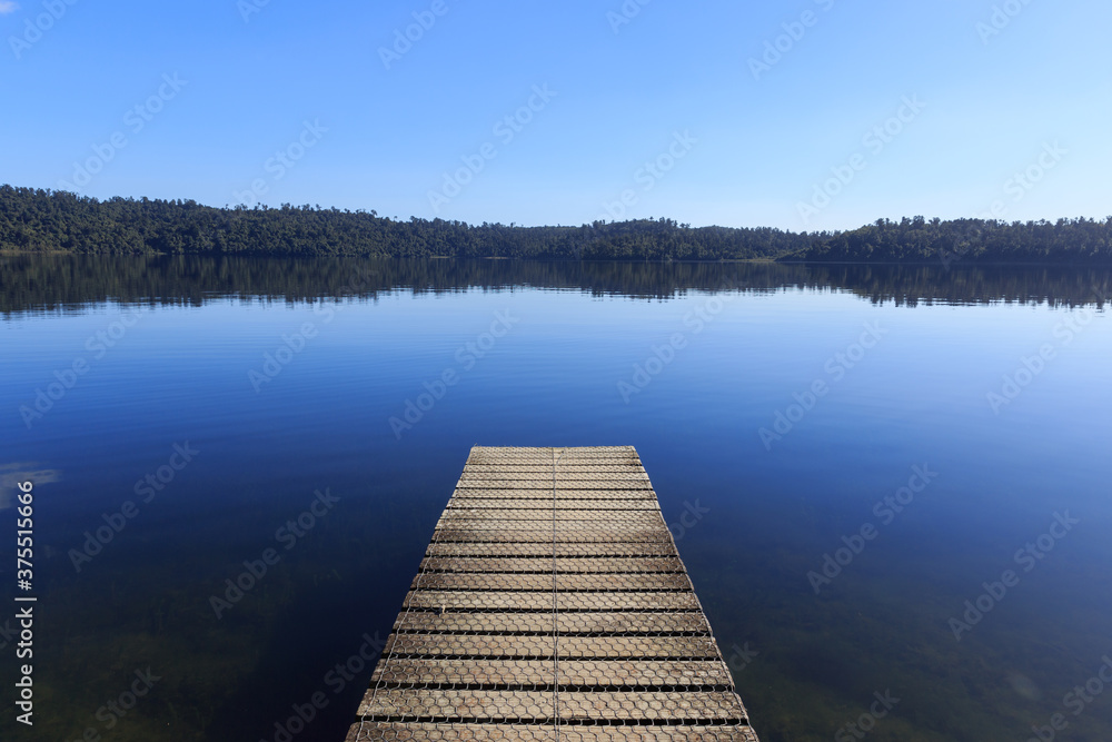 Wall mural wooden pier in the morning at calm mirror lake with mountain background in new zealand.