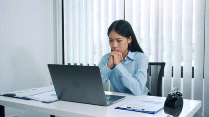 Stress young asian woman is thinking about her work and is looking at the laptop computer at the office.